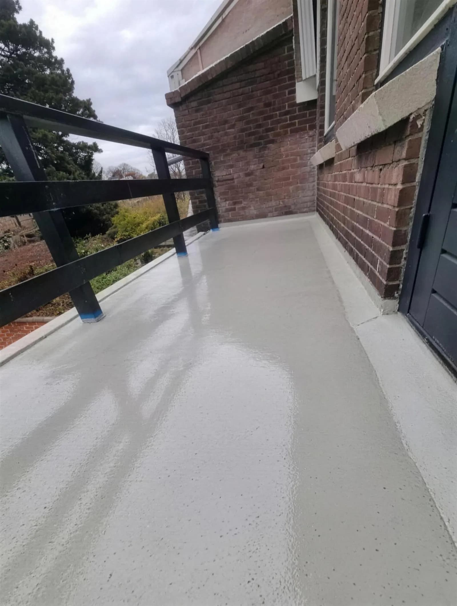 Gerenoveerd balkon met strak gecoate vloer aan een bakstenen gevel